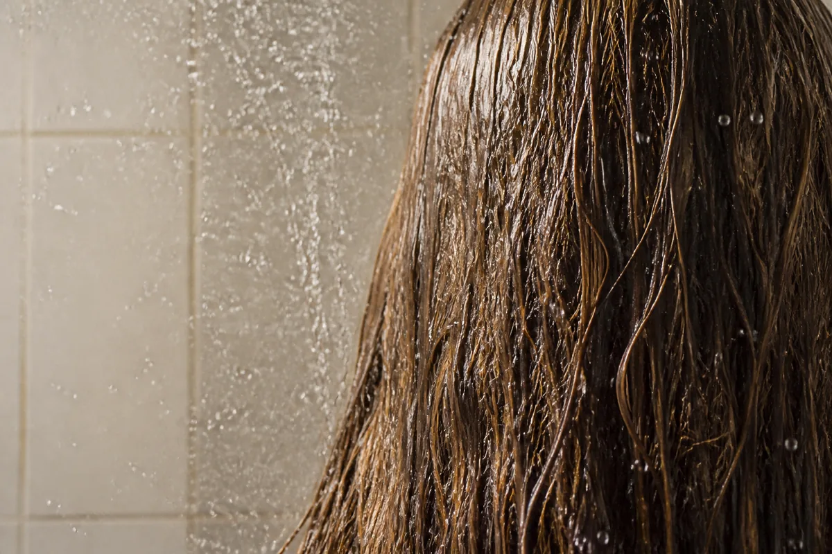 Longueurs de cheveux châtains arrosées d&rsquo;eau claire sous une douche, vue de dos, lumière douce