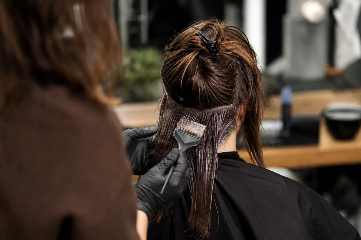 Coiffeuse qui réalise une coloration sur une cliente en salon